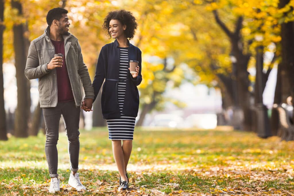 Happy african-american couple with coffee cups walking in park